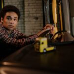 Een chauffeur achter het stuur van een vrachtwagen, omringd door transportmiddelen en een uitzendbureau voor chauffeurs.